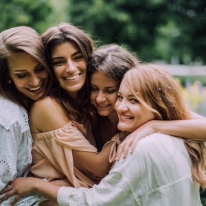 Neljä naista halaa toisiaan kesäisessä maisemassa.
